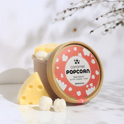 แว็กซ์หอมดีไซน์พิเศษ กลิ่น Caramel Popcorn รูปทรงป๊อปคอร์นและเนยแข็ง วางตกแต่งคู่กับถ้วยคราฟท์ในมุมที่มีแสงธรรมชาติและเงาของกิ่งไม้แบบ Dalayla